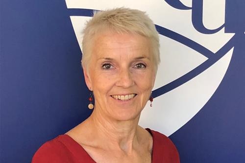 A woman with short blonde hair and dangly earrings smiles.