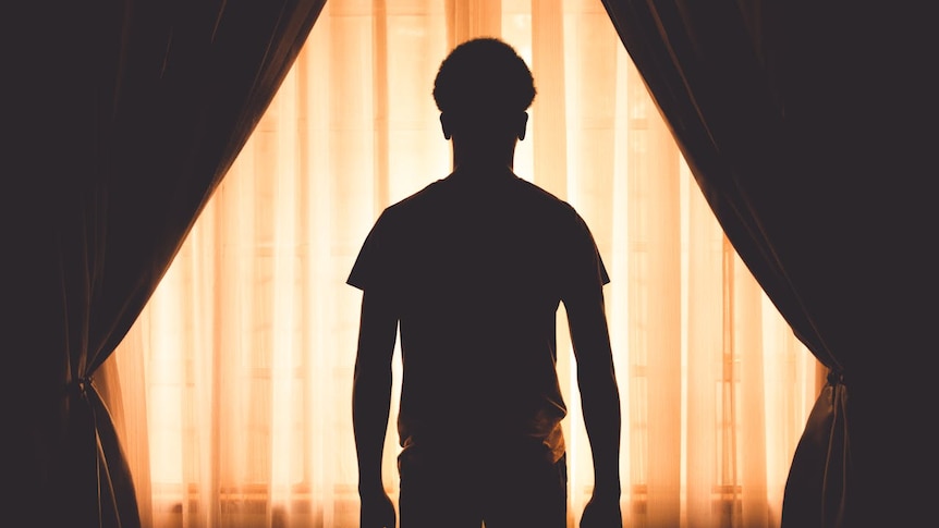 A man stares through a window with a curtain in front of it