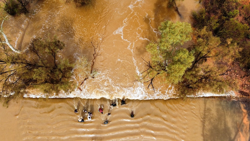 Aerial photo of a group of people sitting on a wall in floodwaters
