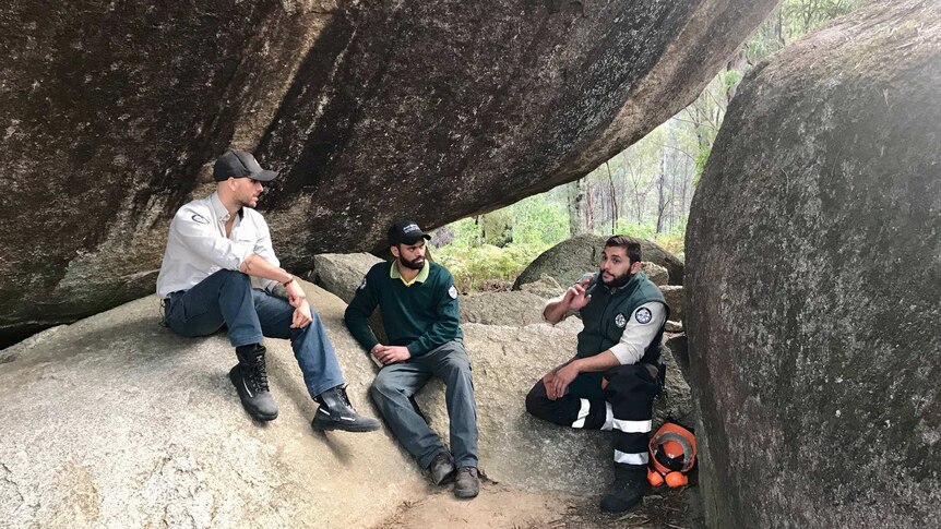 Three Indigenous rangers sit under a rock.