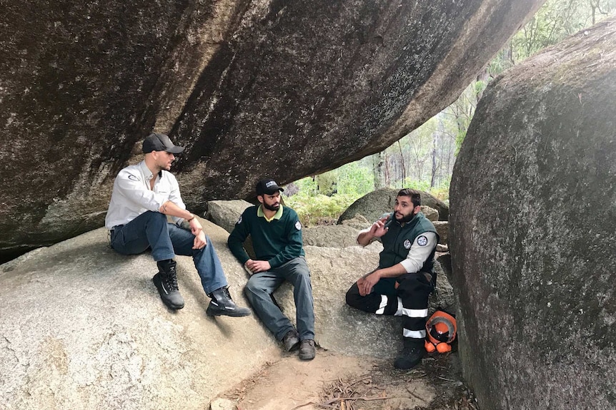 Three Indigenous rangers sit under a rock.