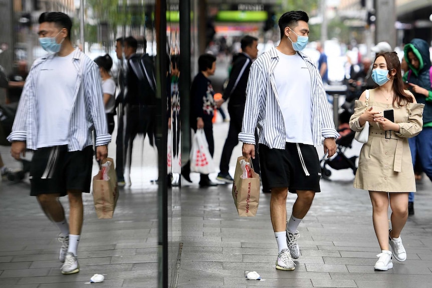 a couple walking down a shopping strip wearing masks