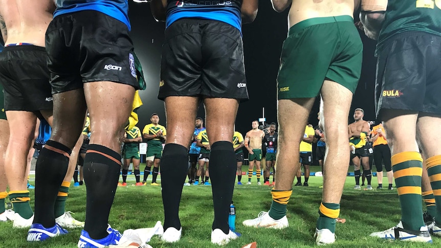 Photo shows men standing around in a circle after a rugby match.
