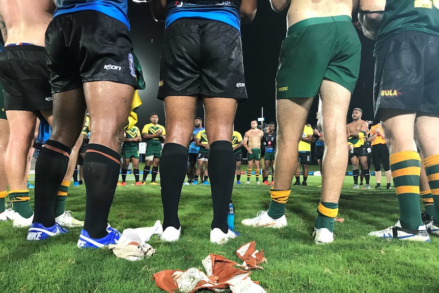 Photo shows men standing around in a circle after a rugby match.