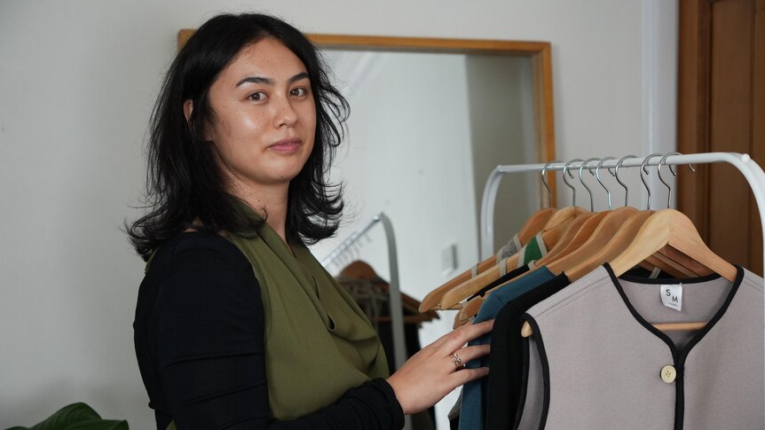 A woman named Shannon Malone stands next to a rack of clothing. 