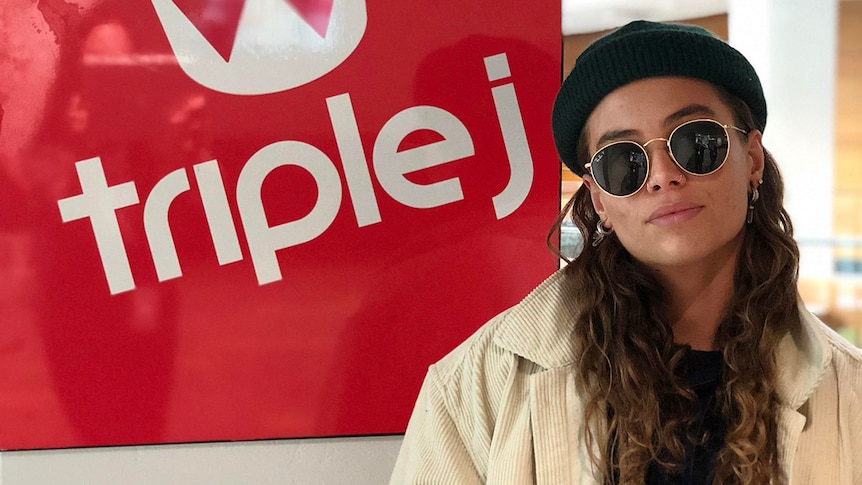Photograph of Tash Sultana standing in front of a triple j lightbox