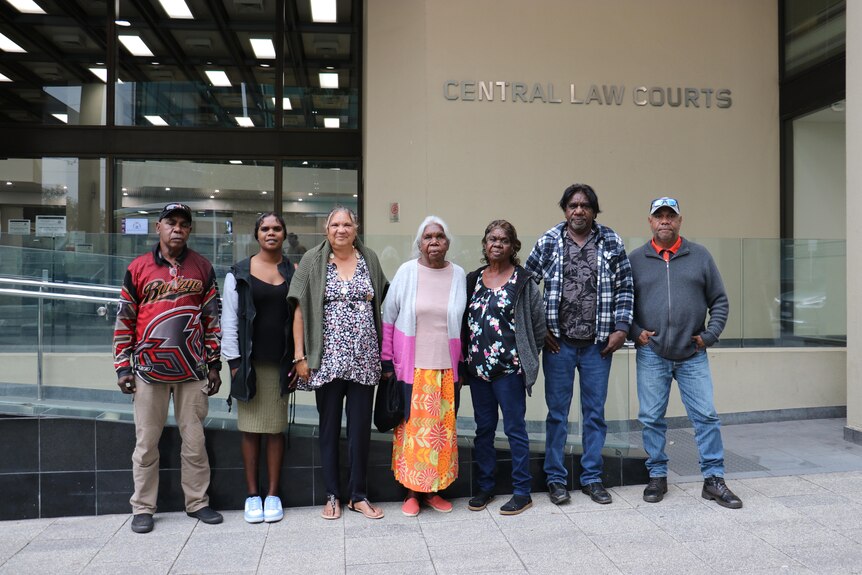 Seven Indigenous men and woman stand side by side posing for a photo outside the Perth Central Law Courts.