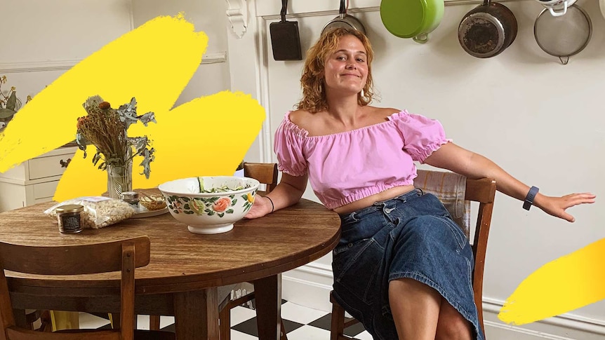 Young woman sitting at a rounnd table in a kitchen, pots and pans hanging up behind her, a stylish rental home.