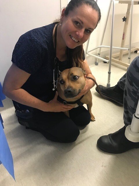 Woman in scrubs sits smiling with dog 