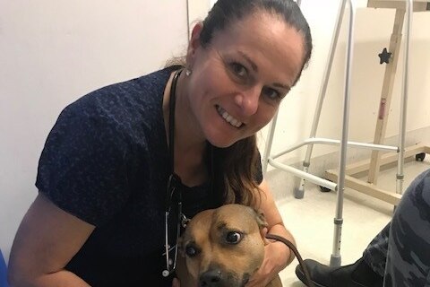 Woman in scrubs sits smiling with dog 