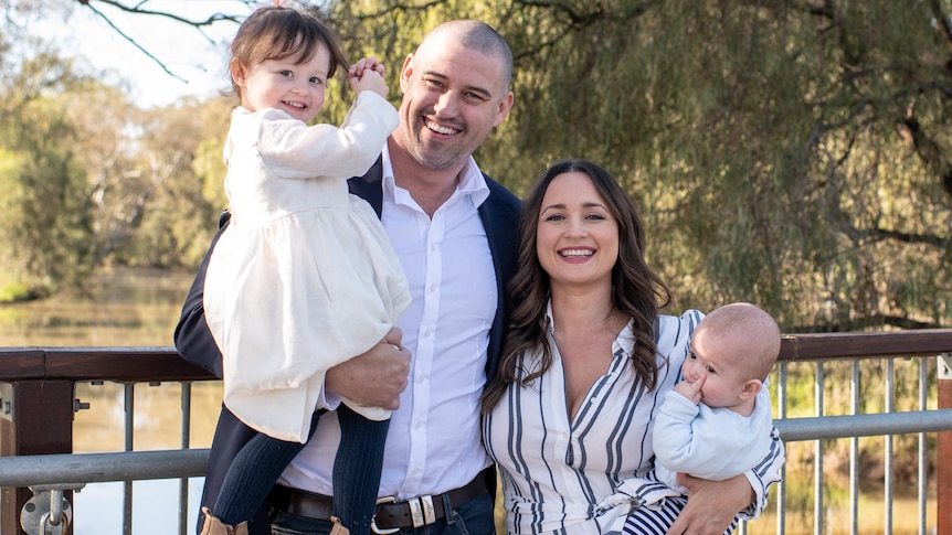 A man and woman smiling, each holding a child in their arms.