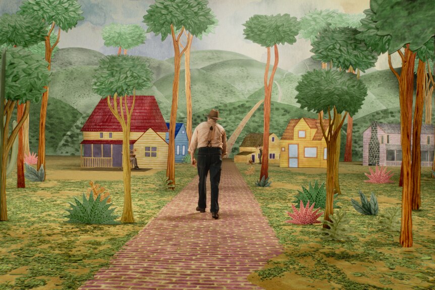 A film still of Joaquin Phoenix in a pilgrim-style outfit walking on a path on an animated set, of trees and suburban houses.