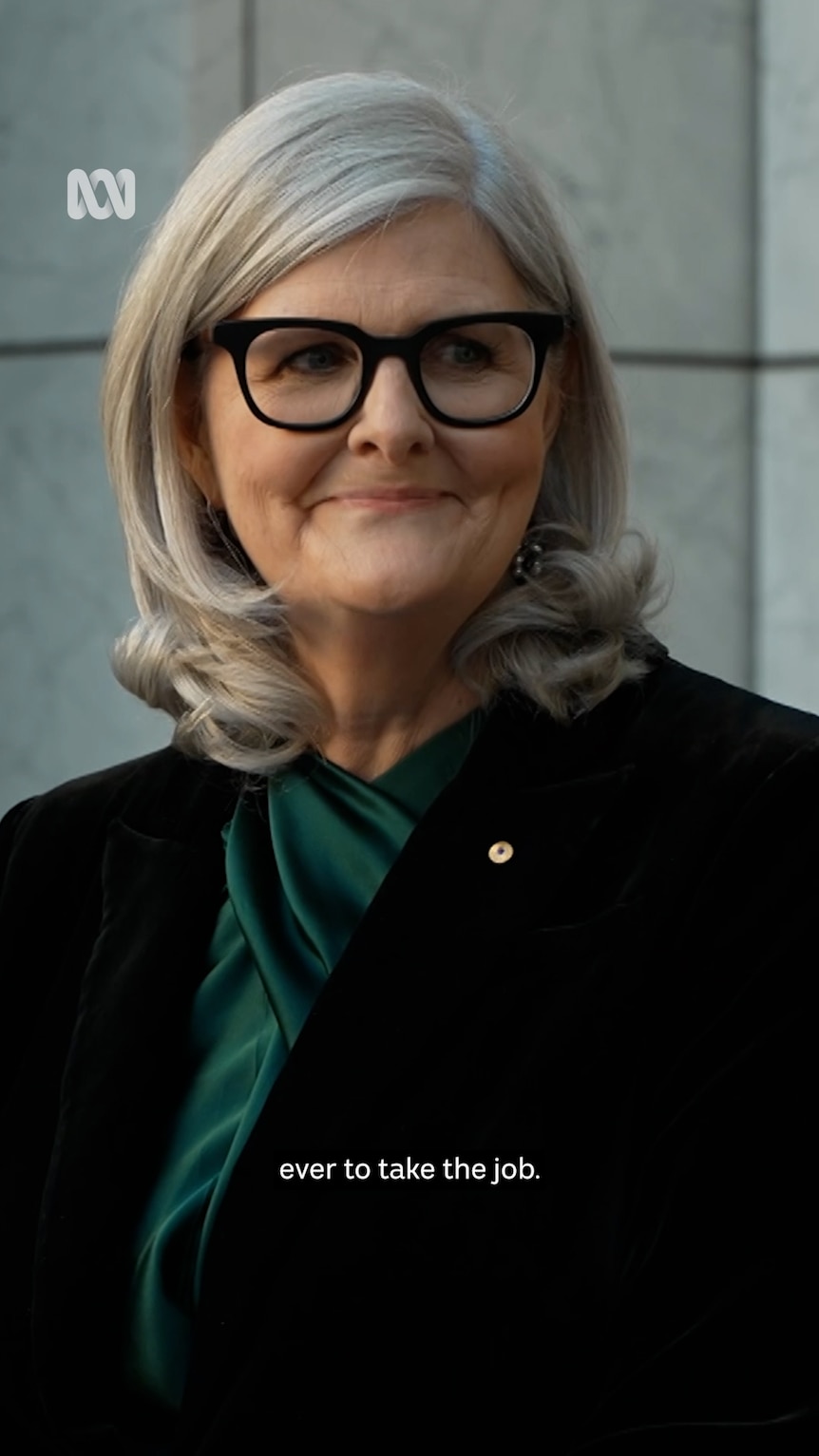 Woman with grey hair and glasses in businesswear smiles  