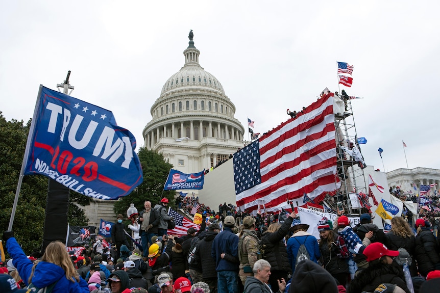 A crowd with flags stands in front of the US Capitol