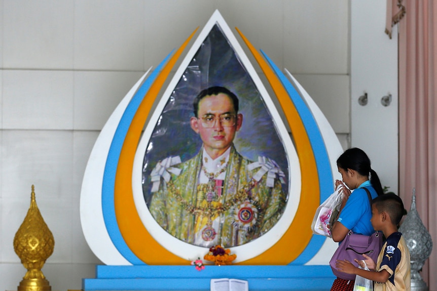 A well-wisher gestures in front of a picture of Thailand's King Bhumibol Adulyadej.