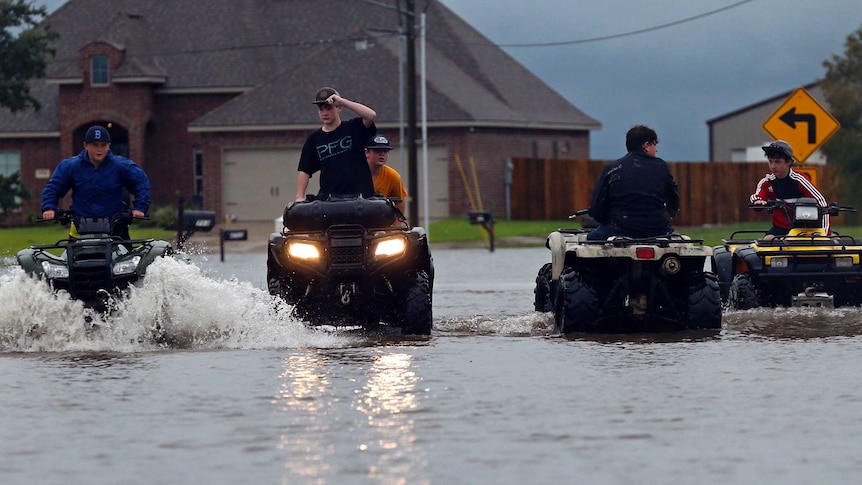 Fout young people ride quad bikes through street flooded with murky waters