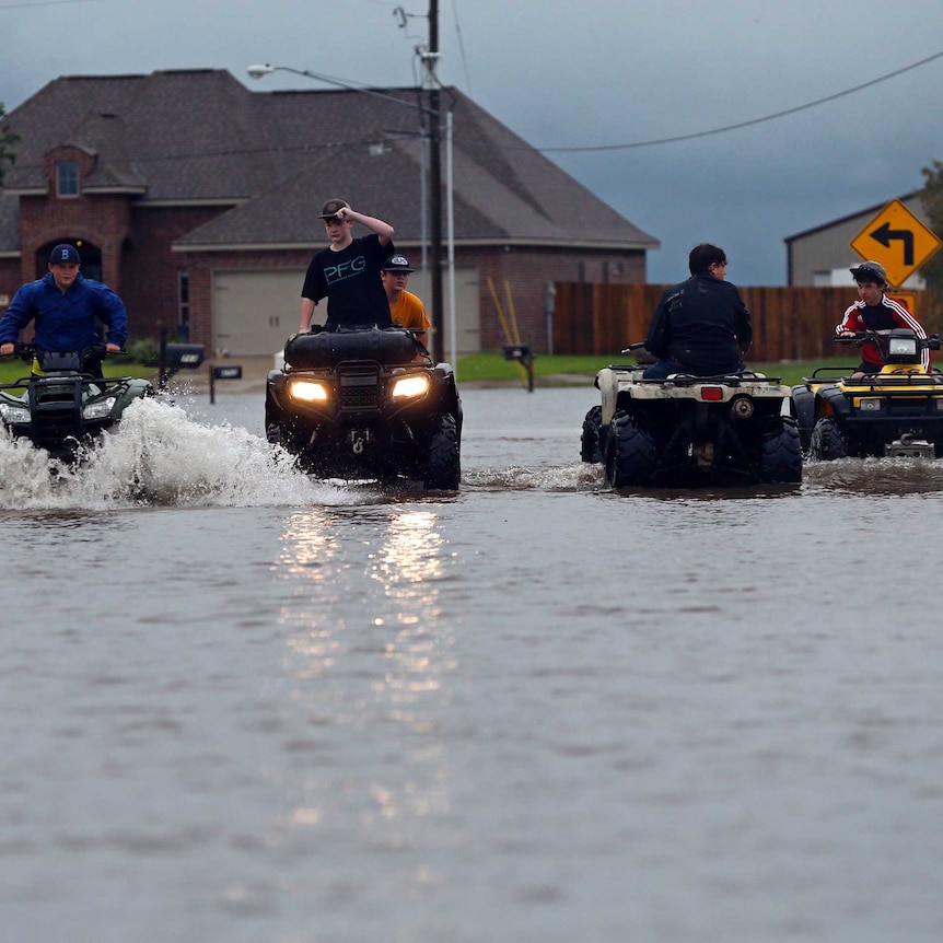 Fout young people ride quad bikes through street flooded with murky waters