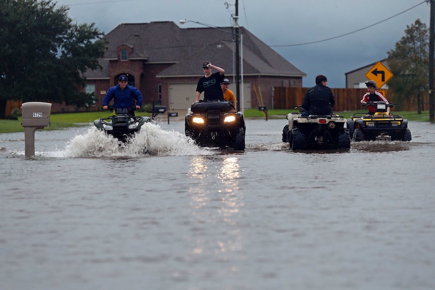 Four young people ride quad bikes through street flooded with murky waters