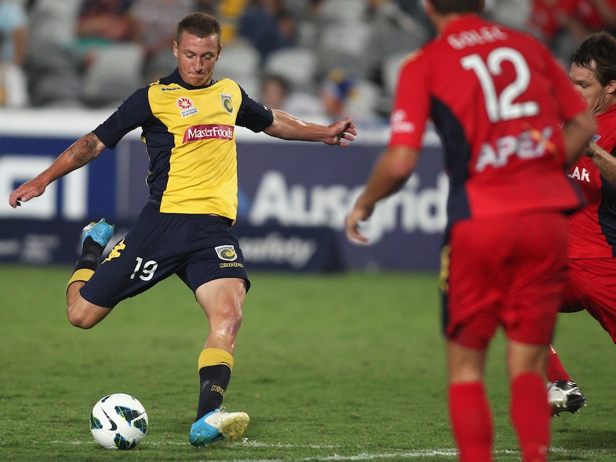 A male soccer player wearing yellow and blue kicks a ball during a game