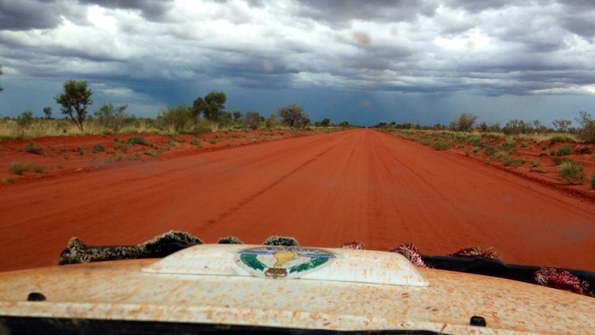 A NT Police vehicle travels on a red dirt road in the Northern Territory.