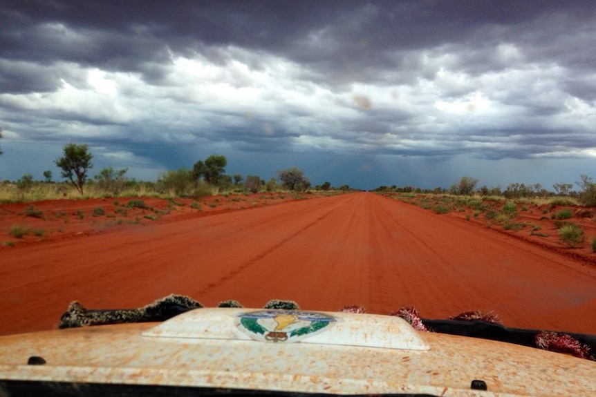 A NT Police vehicle travels on a red dirt road in the Northern Territory.