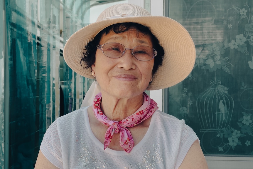 An older South Korean woman in a sunhat, glasses and pink neck scarf 