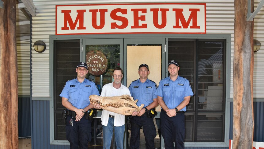 Three police officers stand alongside the museum curater holding the crocodile skiull outside the Museum entry