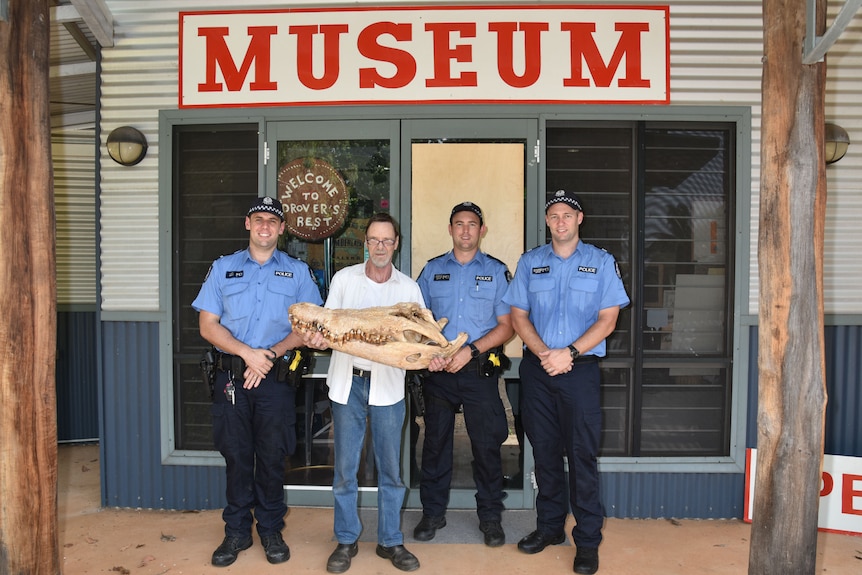 Three police officers stand alongside the museum curater holding the crocodile skiull outside the Museum entry