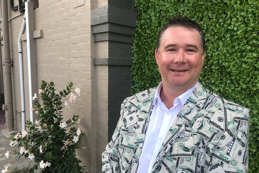 Shane Bradbury smiling at Brisbane racecourse wearing a jacket with US dollar bills design