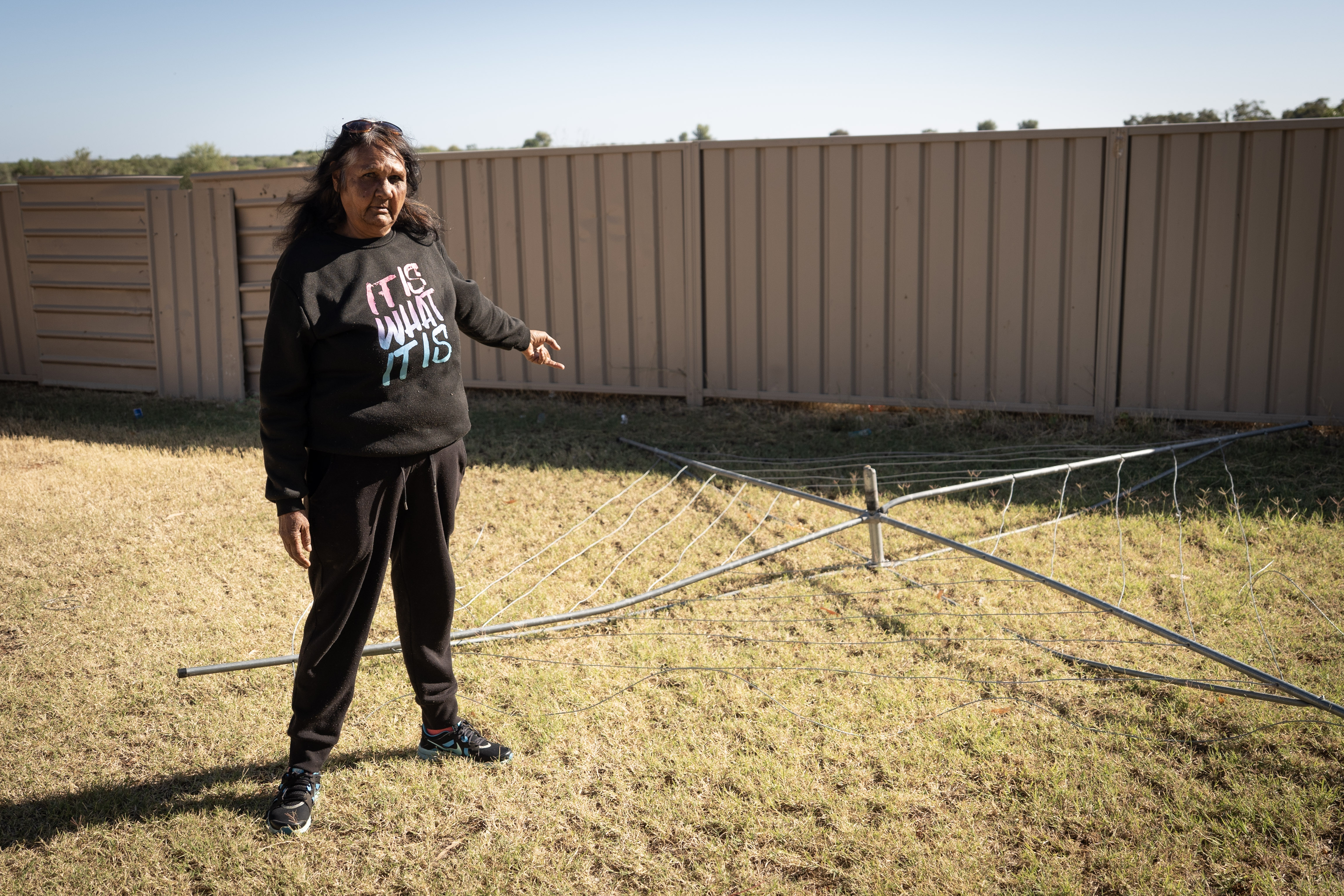 A woman points to a broken clothes hoist lying on the ground.
