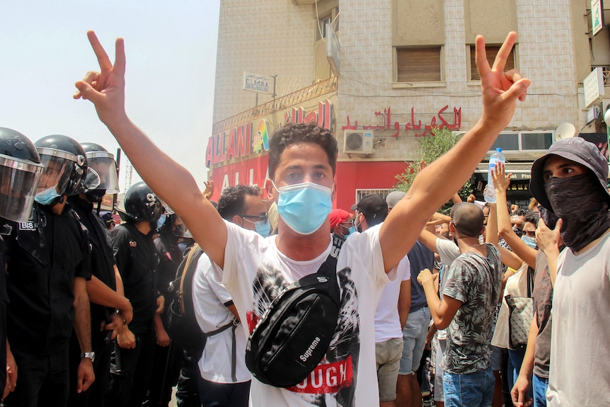 A demonstrator flashes victory sings as he faces Tunisian police officers during a demonstration