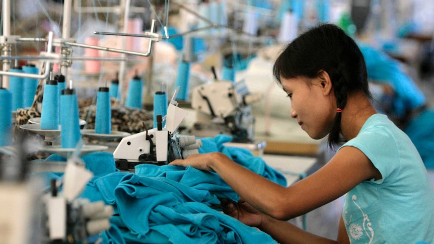 A woman works on a pile of clothes at a sewing machine in a factory