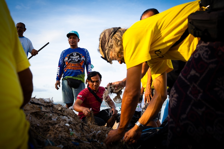 A group of people pick up trash from a Bali beach.