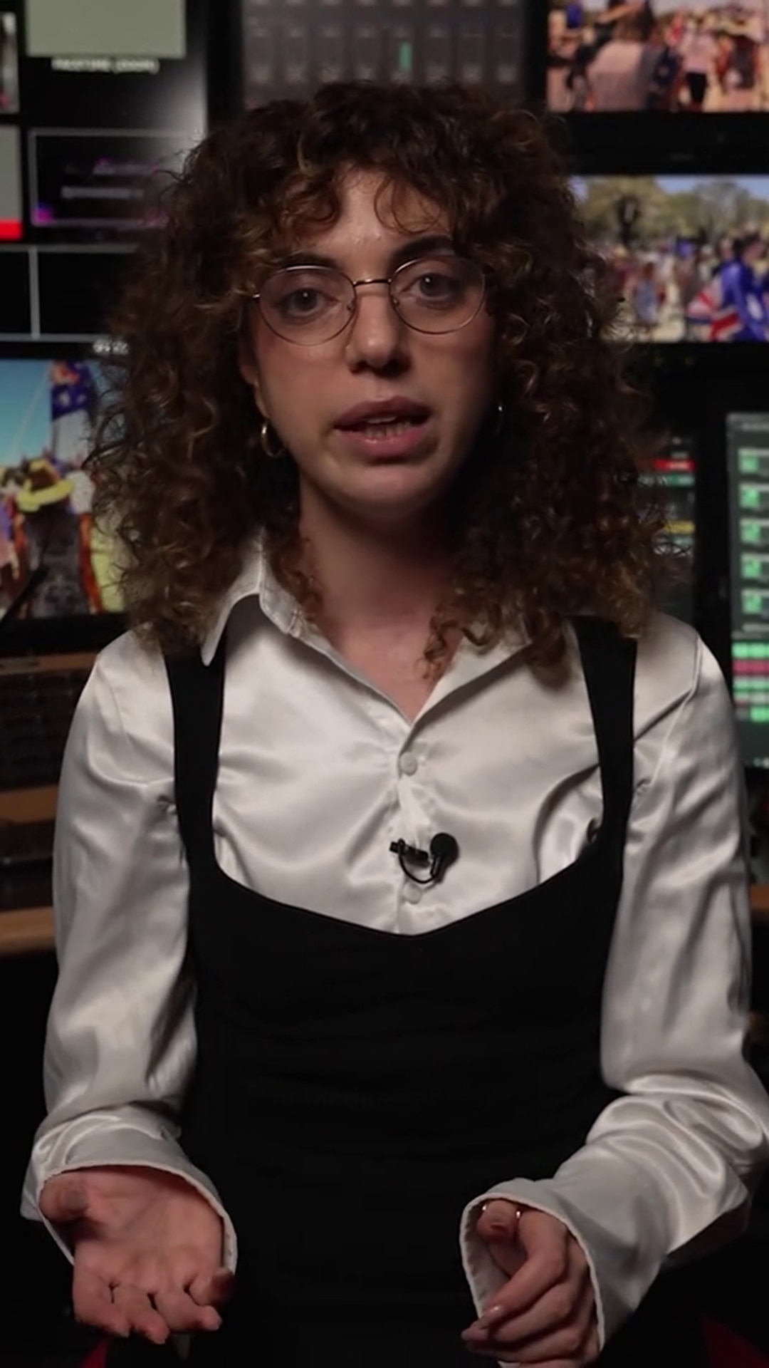 Maryanne Taouk, dressed in a shiny white blouse and dark overalls, appears before studio monitors 