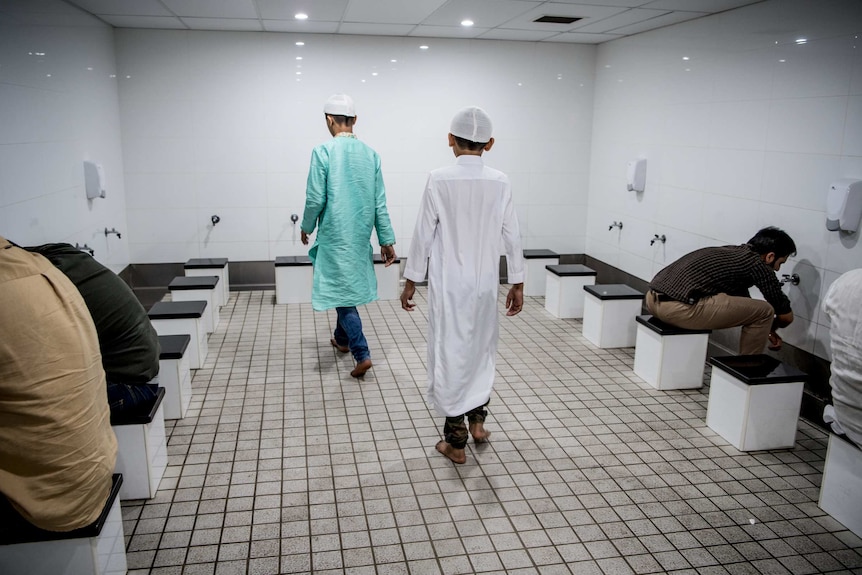 Two young boys walk into a stark white communal washroom.