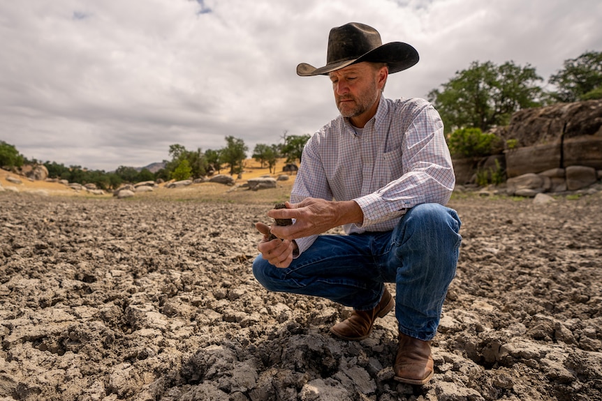 A man in a cowboy hat crouches in a very dry creek bed 
