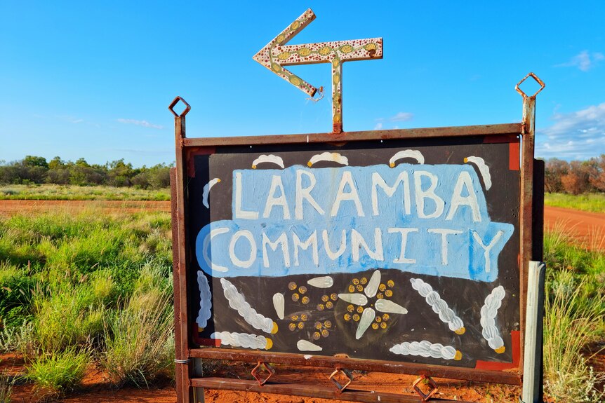 A sign reading 'Laramba Community' points to the left. Red dirt and bush is behind.