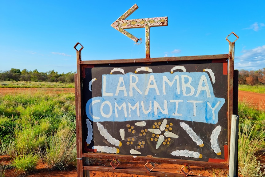 A sign reading 'Laramba Community' points to the left. Red dirt and bush is behind.