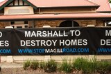 A banner reading Marshall to Destroy Homes is hung on the fence of a stately sandstone house.