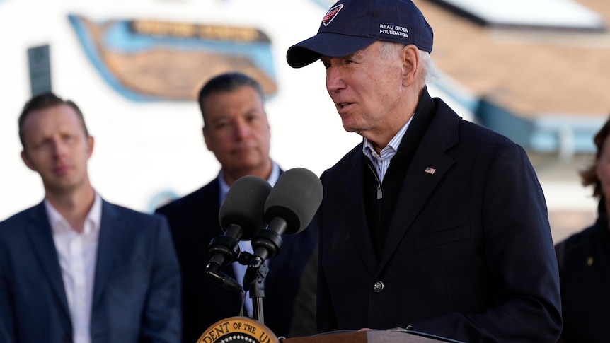 Joe Biden, wearing a hat, speaks at a lectern.
