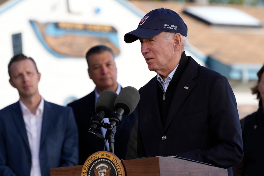 Joe Biden, wearing a hat, speaks at a lectern.