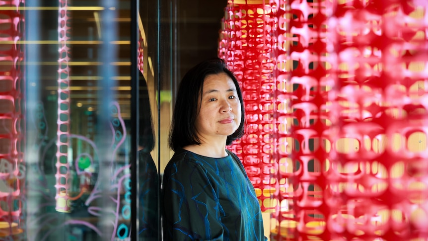 Jenny standing between the window of her store and her art installation of red lanterns.