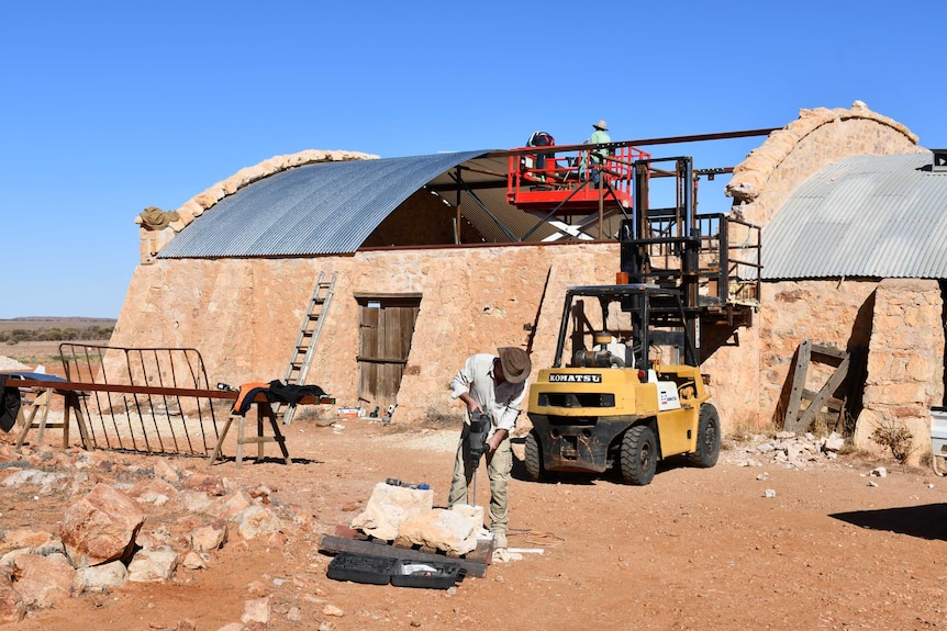 An old woodshed being restored by people using scissor lifts and forklifts.