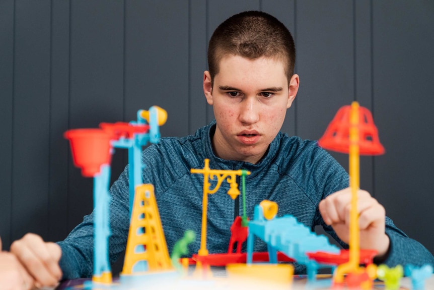 A teenage boy sits at a table playing with a plastic toy set.