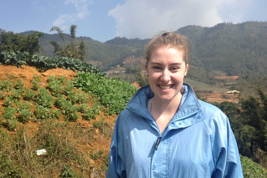 Research Associate Nikki Dumbrell wearing a blue jacket in a broccoli crop of a steep cliff in Vietnam