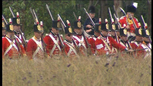 Olden day soldiers with guns stand at ease in tall grass
