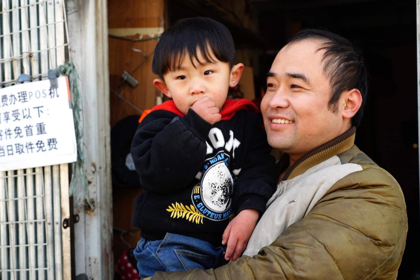 Migrant worker Wang Zhonggan smiles as he holds his young in his arms.