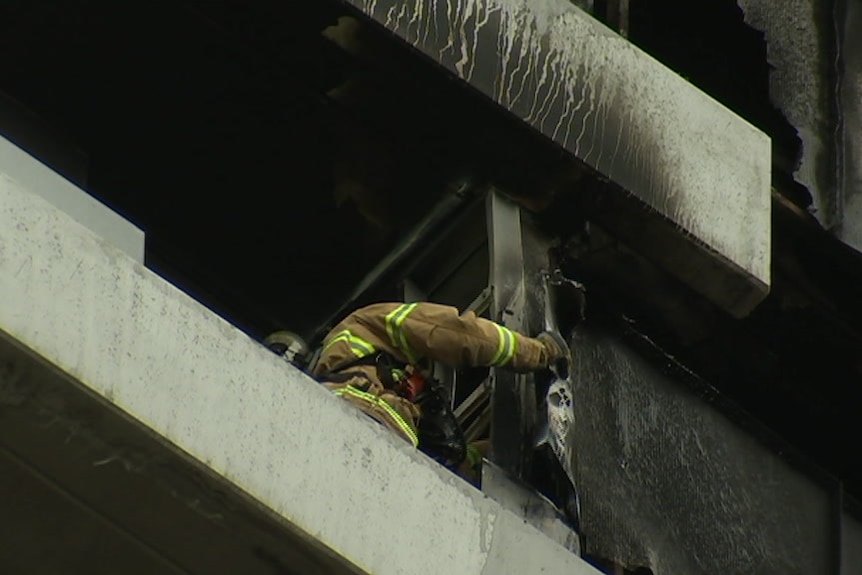 A firefighter handles charred materials from the balcony of an apartment.