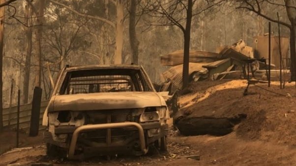 Burnt white utility vehicle and the remains of a house in smoky bushland