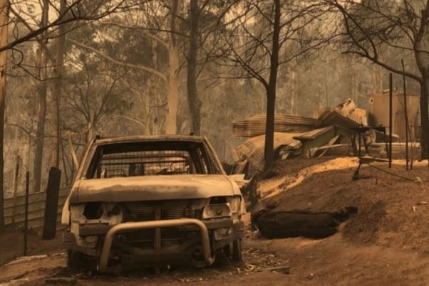 Burnt white utility vehicle and the remains of a house in smoky bushland